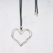 Trendige silberne Herzkette mit Schnurband und dem Schriftzug ‚LOVE‘. Der 90er-Jahre-inspirierte Schmuck bietet eine verspielte und kraftvolle Note, mit flexibler Verschlussmöglichkeit durch Knoten oder Schlaufe.