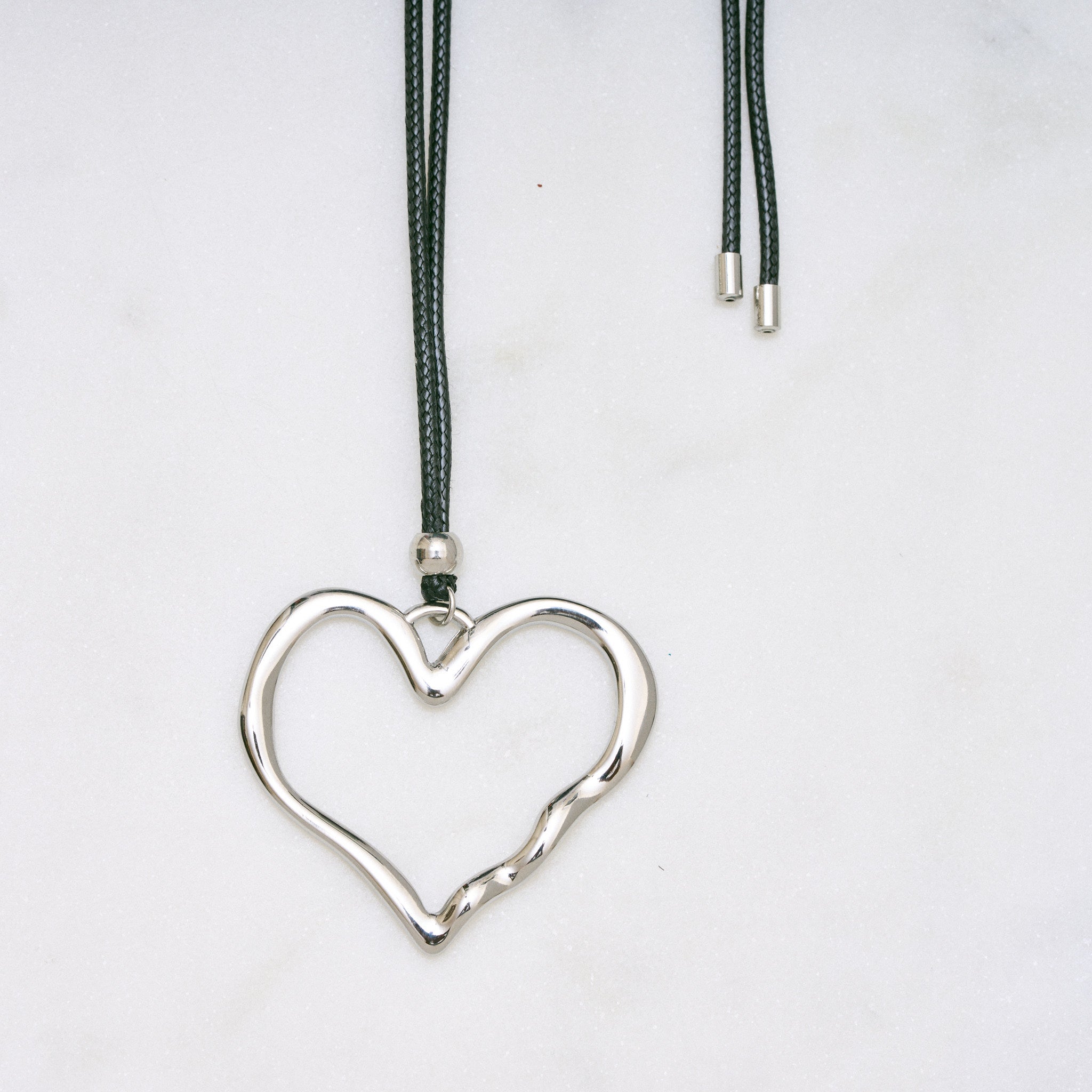 Trendige silberne Herzkette mit Schnurband und dem Schriftzug ‚LOVE‘. Der 90er-Jahre-inspirierte Schmuck bietet eine verspielte und kraftvolle Note, mit flexibler Verschlussmöglichkeit durch Knoten oder Schlaufe.