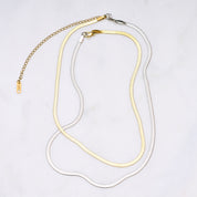 Zwei Snake Mini Ketten in Silber und Gold miteinander verbunden, die sich wie eine zarte Schlange um den Hals legen und im Licht glitzern. Die Bi-Color-Kombination betont den Trend-Look.