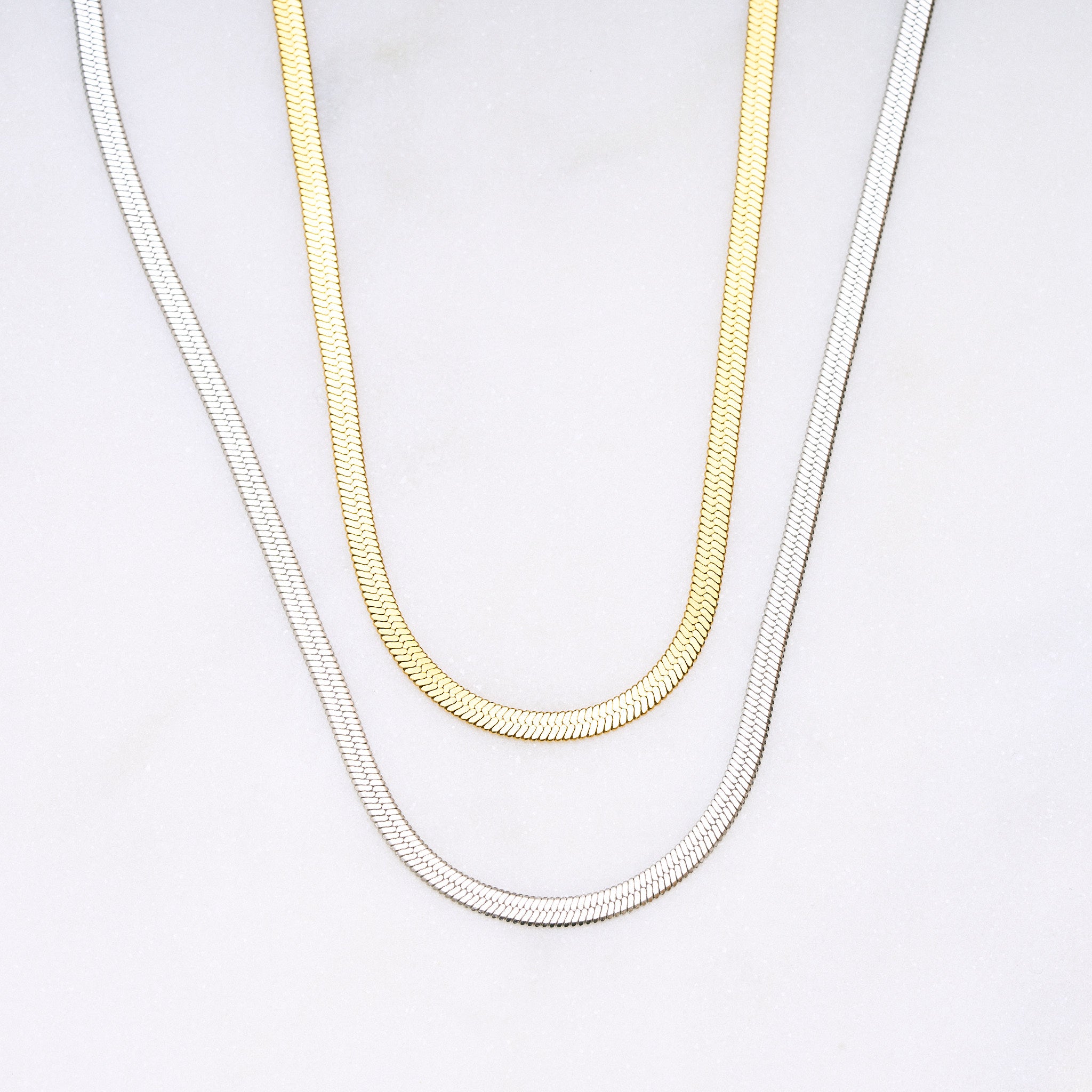 Zwei Snake Mini Ketten in Silber und Gold miteinander verbunden, die sich wie eine zarte Schlange um den Hals legen und im Licht glitzern. Die Bi-Color-Kombination betont den Trend-Look.