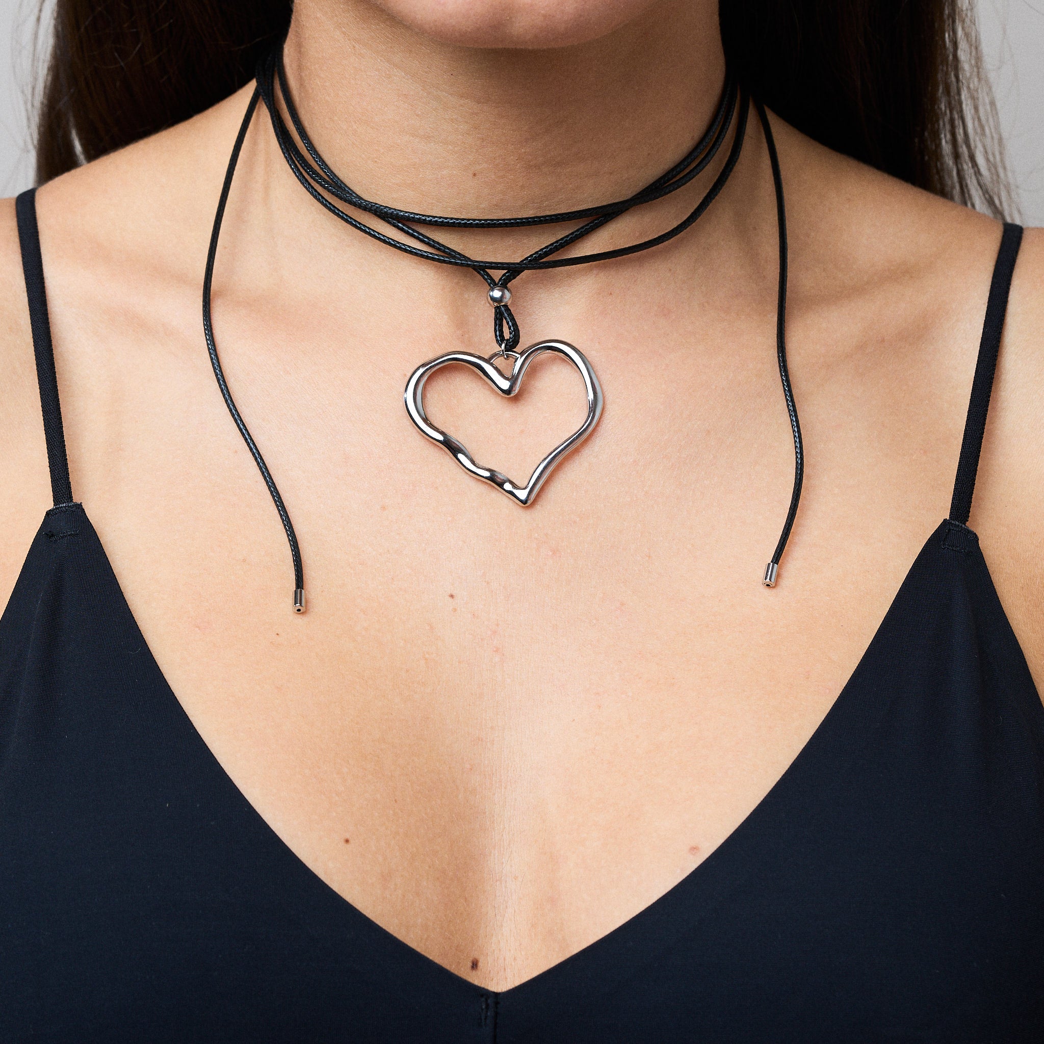 Trendige silberne Herzkette mit Schnurband und dem Schriftzug ‚LOVE‘. Der 90er-Jahre-inspirierte Schmuck bietet eine verspielte und kraftvolle Note, mit flexibler Verschlussmöglichkeit durch Knoten oder Schlaufe.